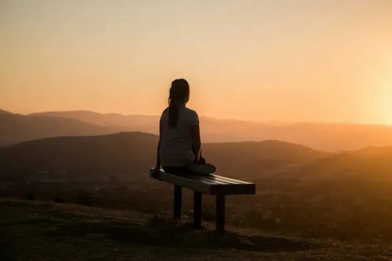 Person sitting peacefully at sunset overlooking mountains